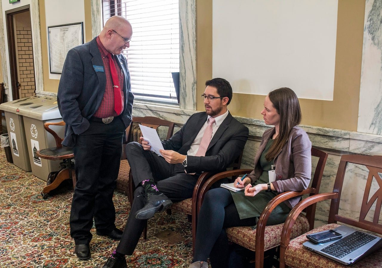 A group of legislators sit in chairs.
