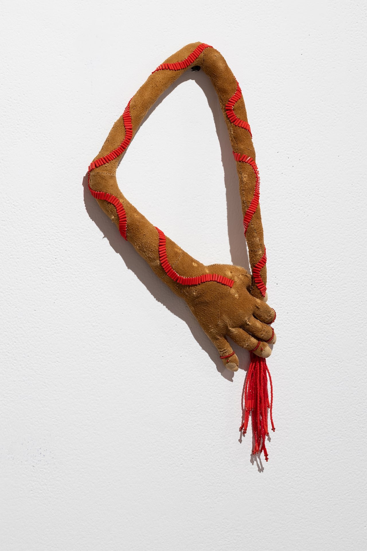 Artwork featuring a hand and arm bending around itself, crafted from caribou hide, beaver fur, and beads.
