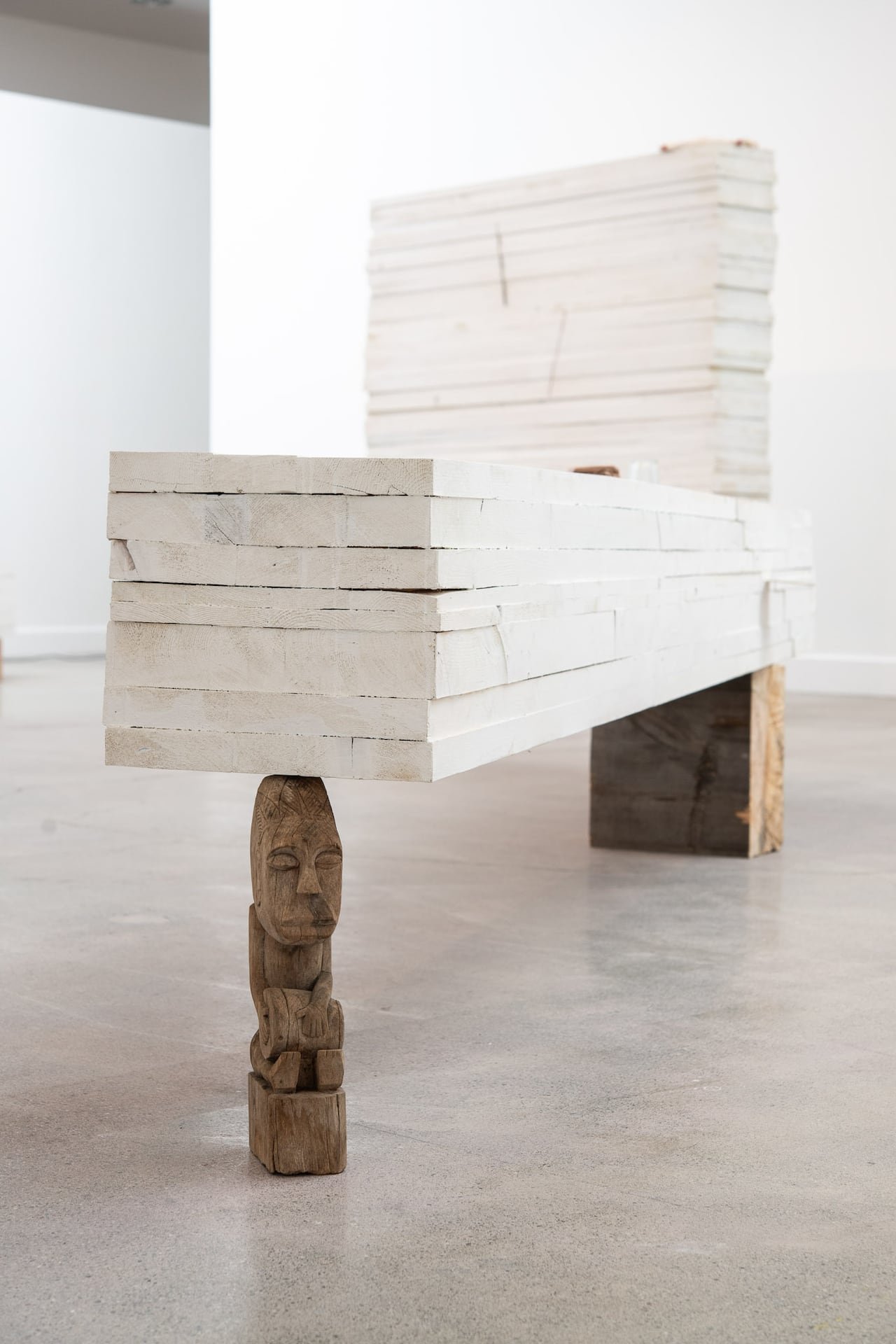 Artwork depicting a grey flat material balanced on a small carved sculpture.
