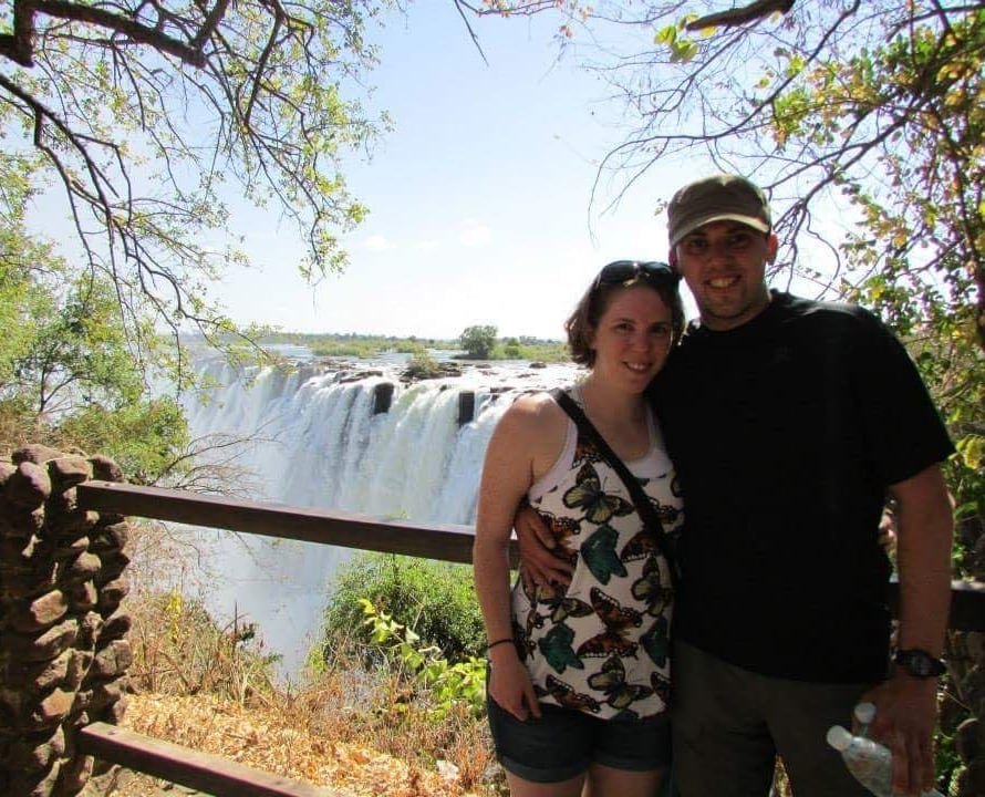 default-70 A man and woman pose for a photo while standing near a waterfall.